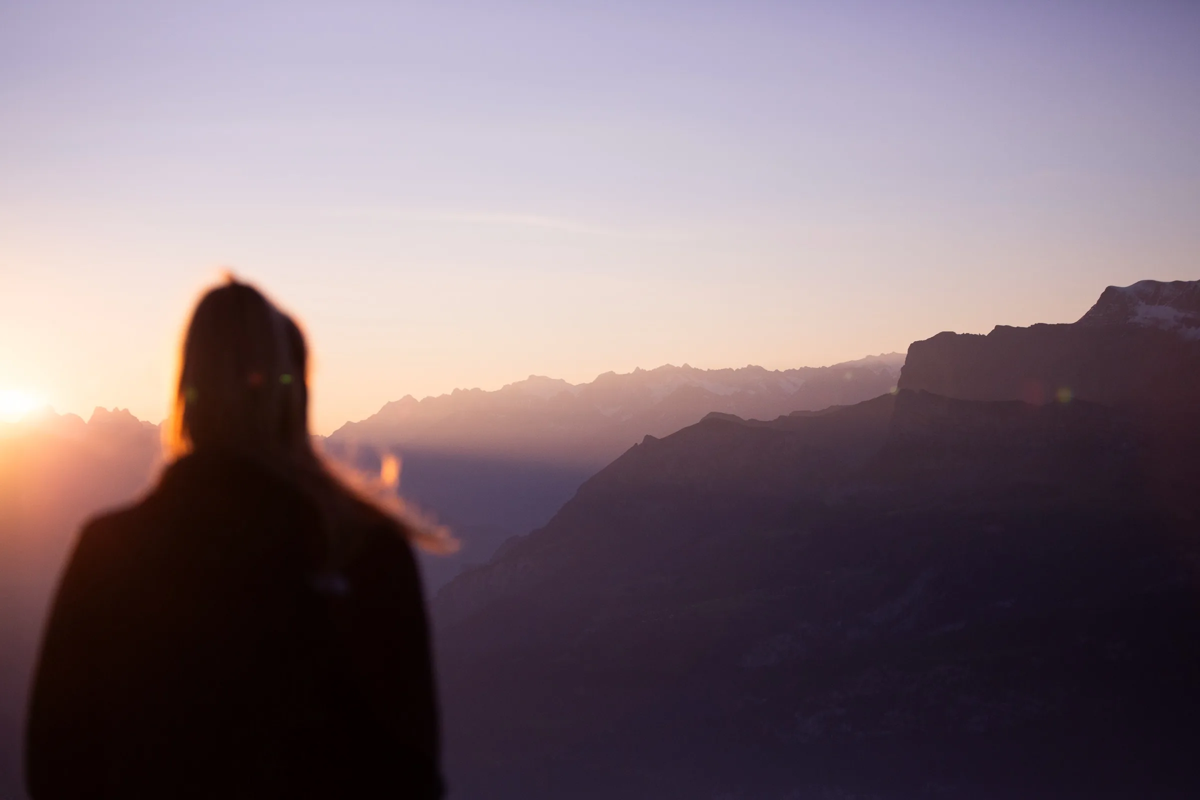 Person blickt bei Sonnenaufgang über eine Bergkette